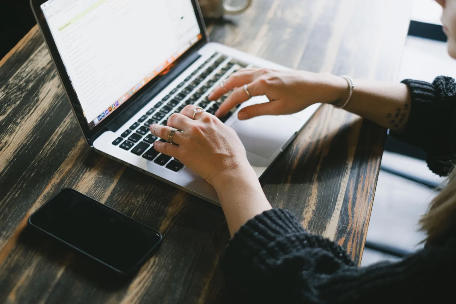 Hands typing on a laptop next to a smartphone while processing an online job application