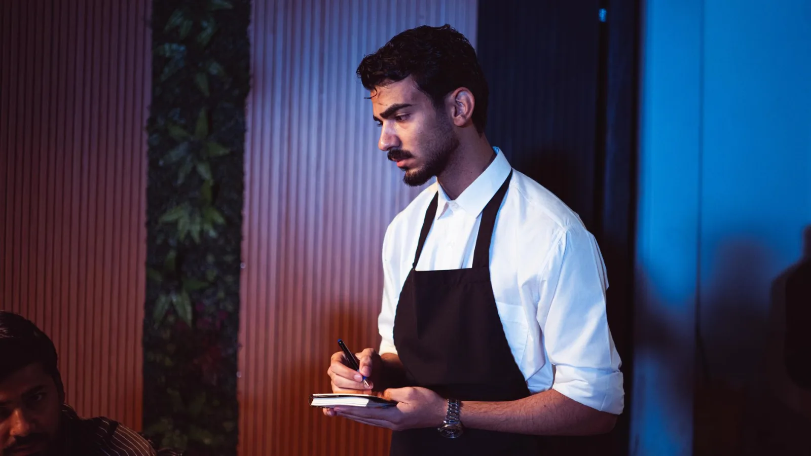 Waiter in an apron taking an order in a restaurant dining room during service