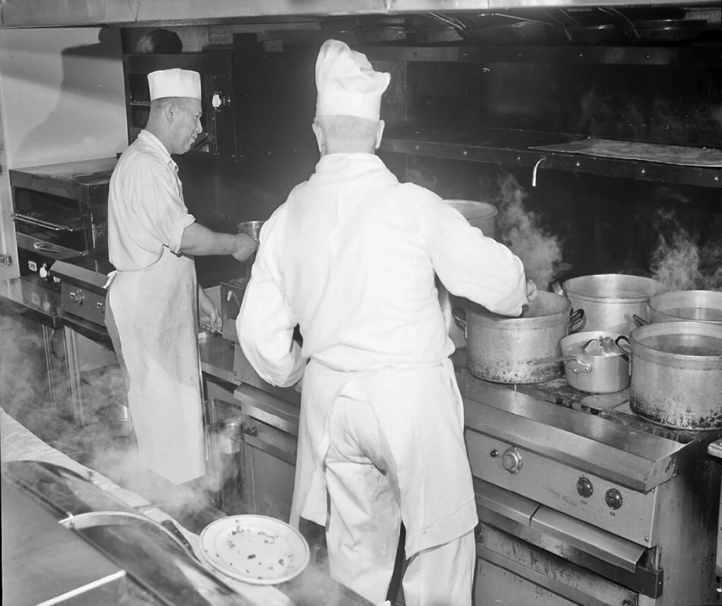 Deux cuisiniers en toque au travail devant les fourneaux d'une cuisine de restaurant